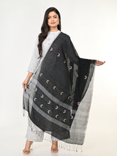 A woman modeling a black and white handloom jamdani cotton dupatta with intricate patterns and pompoms, wearing a white shirt and light-colored pants.
